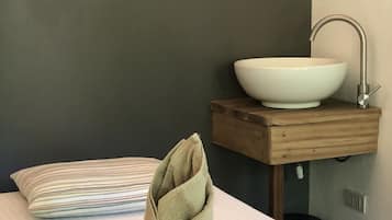 Une salle de bain avec un lavabo blanc posé sur un meuble en bois, une serviette sur le lit et un coussin à rayures.
