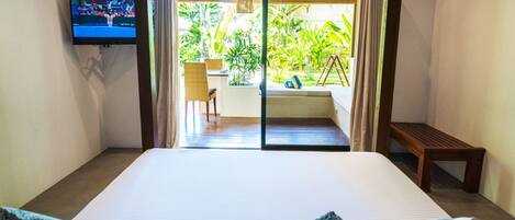 A hotel room with a large bed, a TV mounted on the wall, and a sliding glass door leading to an outdoor area with a chair and a table.