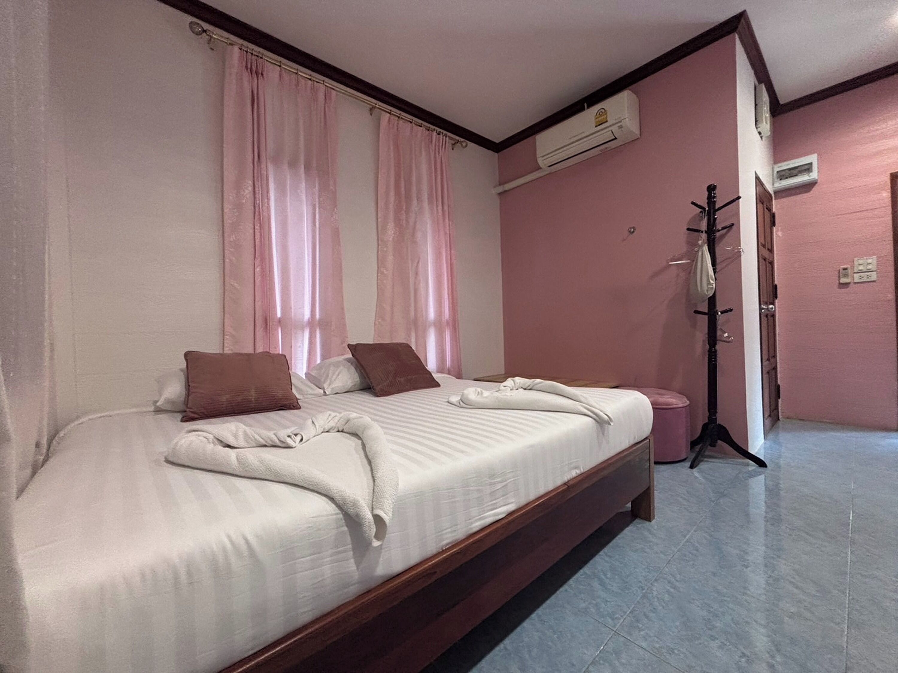 A double bed with a wooden frame, two pillows, and a white blanket. There is a wooden floor and a wall-mounted air conditioner.