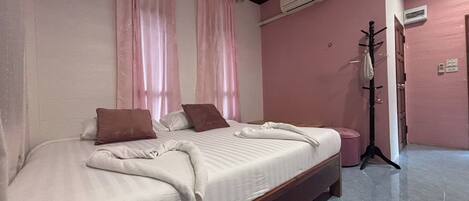 A double bed with a wooden frame, two pillows, and a white blanket. There is a wooden floor and a wall-mounted air conditioner.