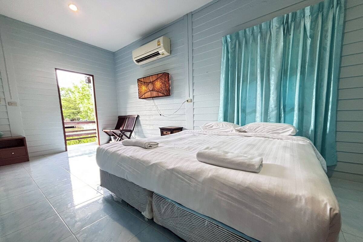A modern bedroom with a large bed, a desk, and a chair. There is a window with curtains and an air conditioning unit on the wall.