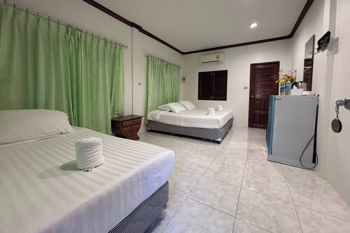 A hotel room with a large bed, a smaller bed, a nightstand, a wardrobe, a mirror, a door, and a refrigerator.