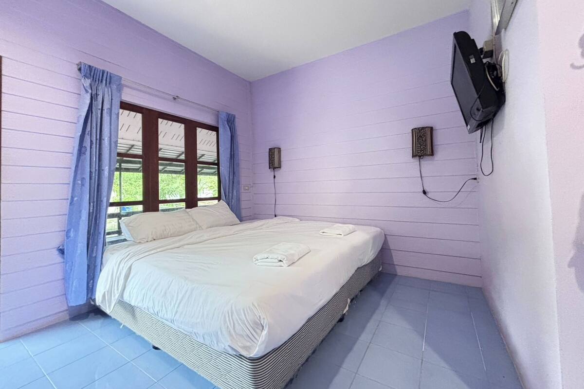A bedroom with a bed, curtains, a window, a wall-mounted TV, and a power outlet.