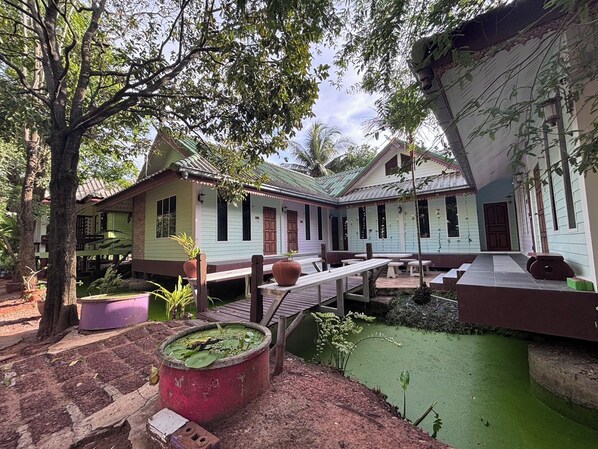 A traditional wooden house with a thatched roof, surrounded by lush greenery and a small pond. - Aioun At Amphawa (Amphawa)
