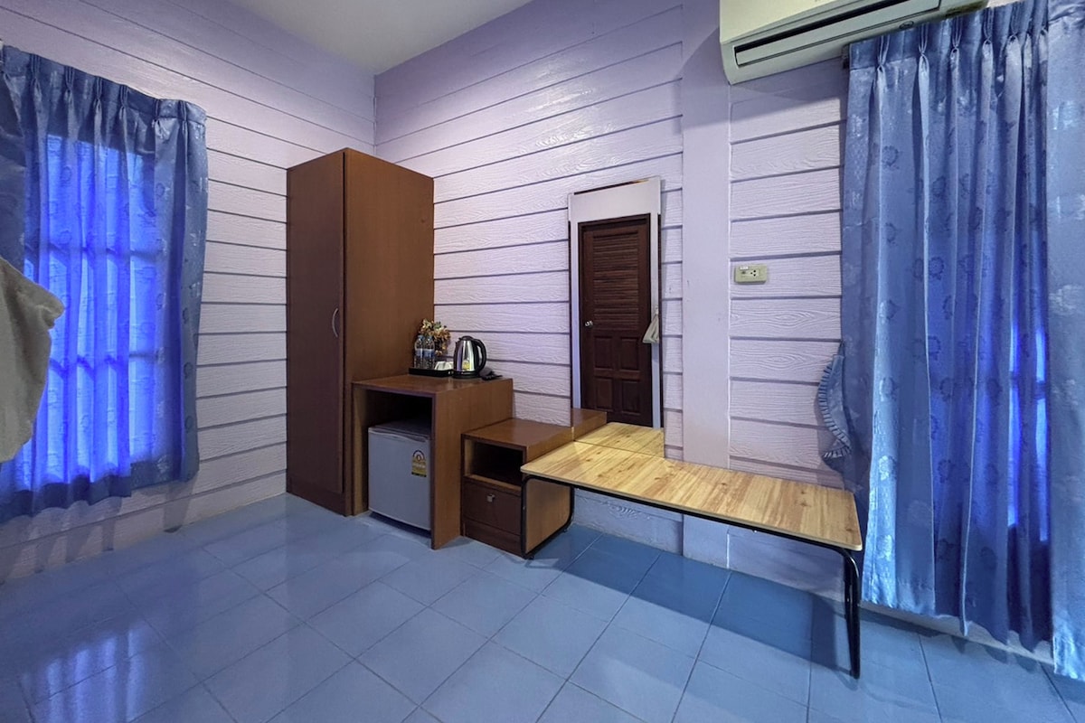 A compact room with a bed, a small desk, a wardrobe, and an air conditioning unit.