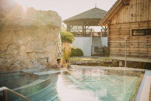 A swimming pool with a wooden cabin and a gazebo in the background. - Avita Resort (Bad Tatzmannsdorf)