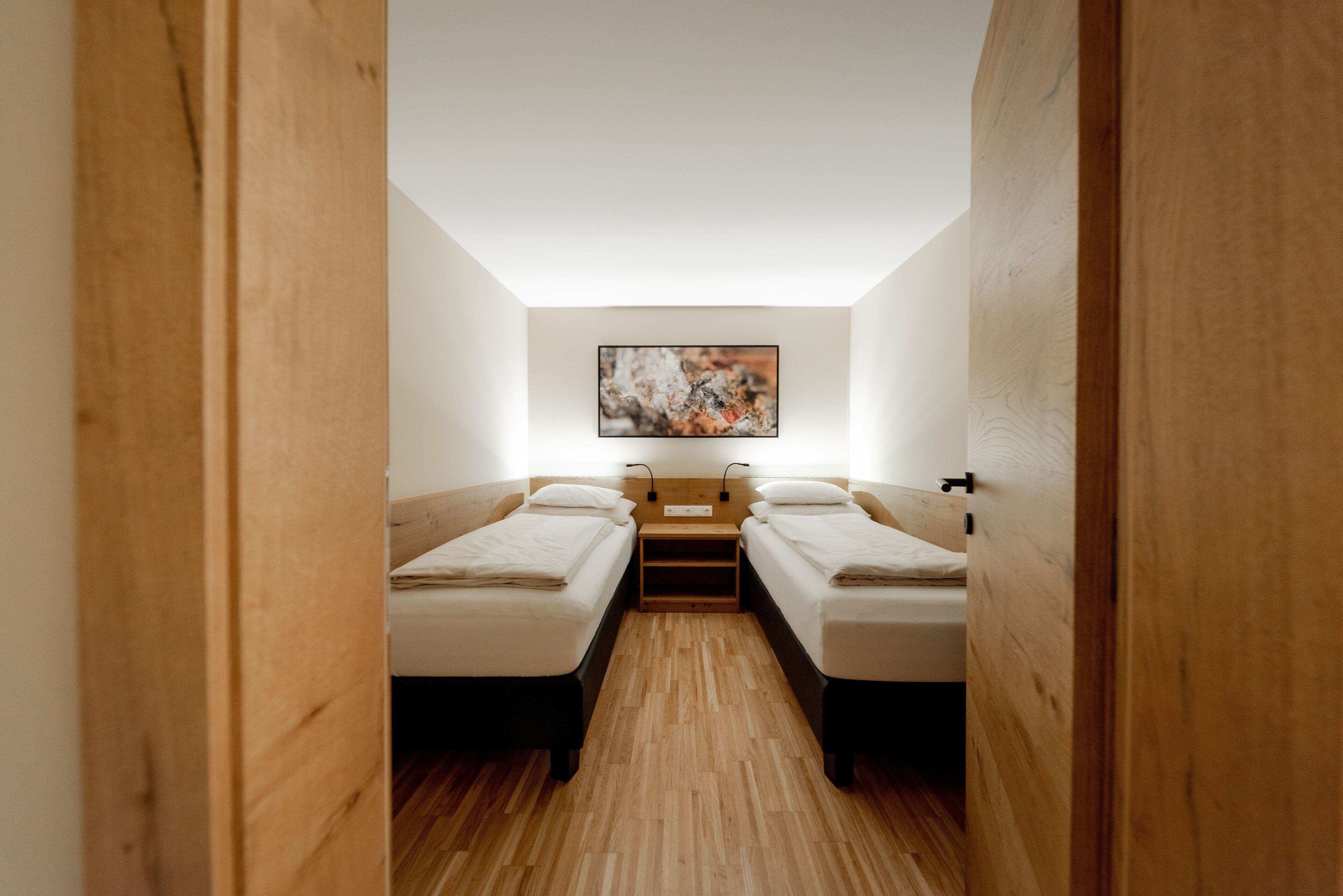 Una habitación pequeña con dos camas individuales, suelo de madera y un cuadro en la pared.