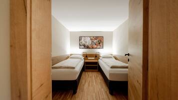 Una habitación pequeña con dos camas individuales, suelo de madera y un cuadro en la pared.