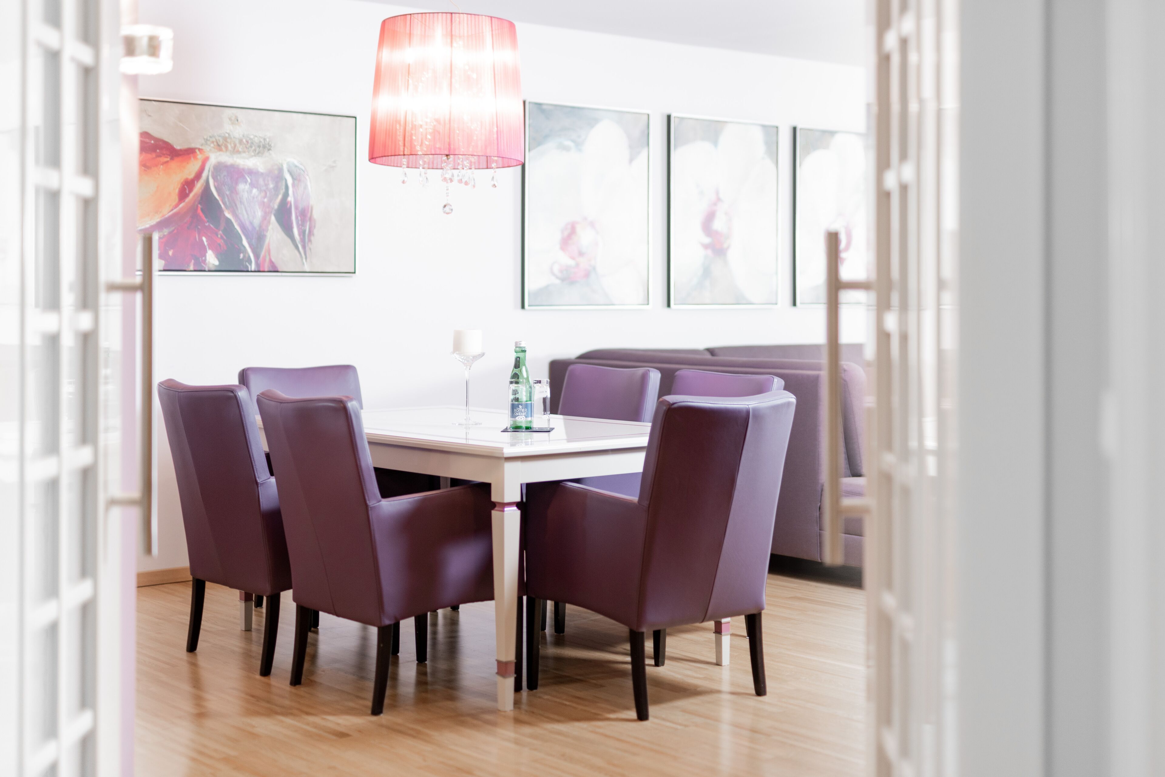 Ein Essbereich mit einem weißen Tisch, violetten Stühlen und einer Kristallleuchter.