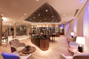 Un moderno vestíbulo de hotel con un mostrador de recepción central, asientos cómodos y una escalera que lleva a los pisos superiores.