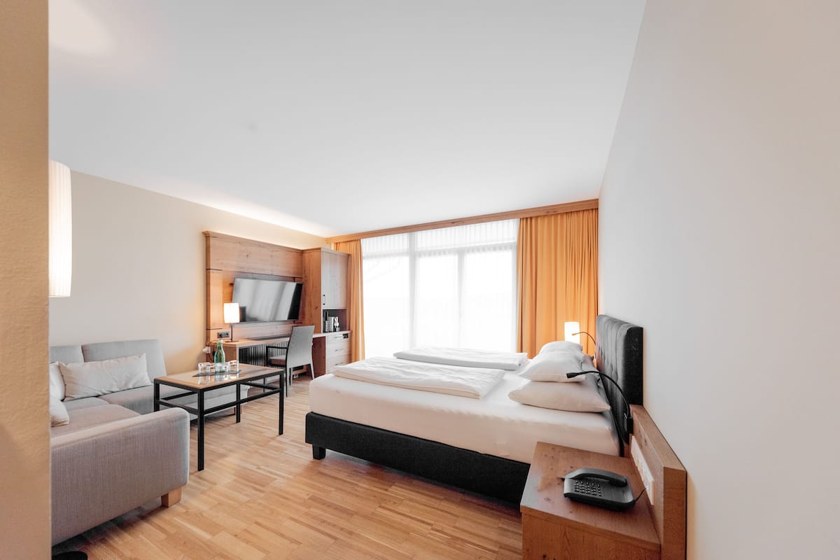 Ein Hotelzimmer mit einem Bett, einem Schreibtisch, einem Stuhl, einem Fernseher und einem Fenster mit Vorhängen.