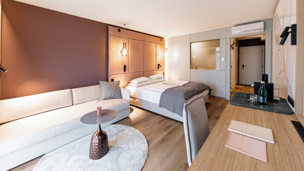 A modern hotel room with a bed, sofa, and a small table with a vase.