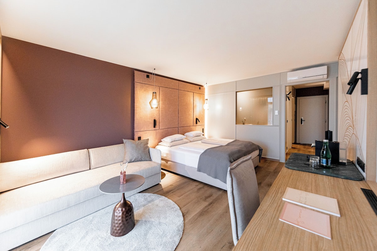 Ein modernes Hotelzimmer mit Bett, Sofa und einem kleinen Tisch mit einer Vase.