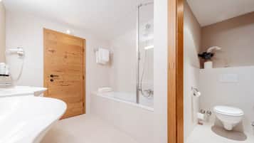 Un baño moderno con puerta de madera, ducha con cerramiento de vidrio, lavamanos blanco y un inodoro.