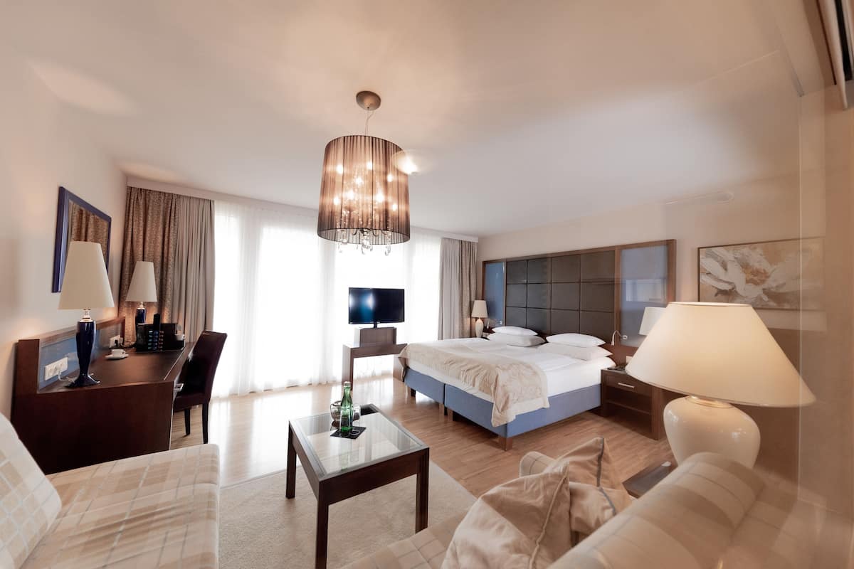 Ein Hotelzimmer mit Bett, Schreibtisch, Fernseher, einer Chandelierleuchtre und einem Sofa.