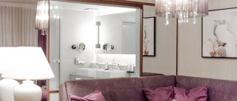 A modern hotel room with a plush purple sofa, a large mirror, and a chandelier.