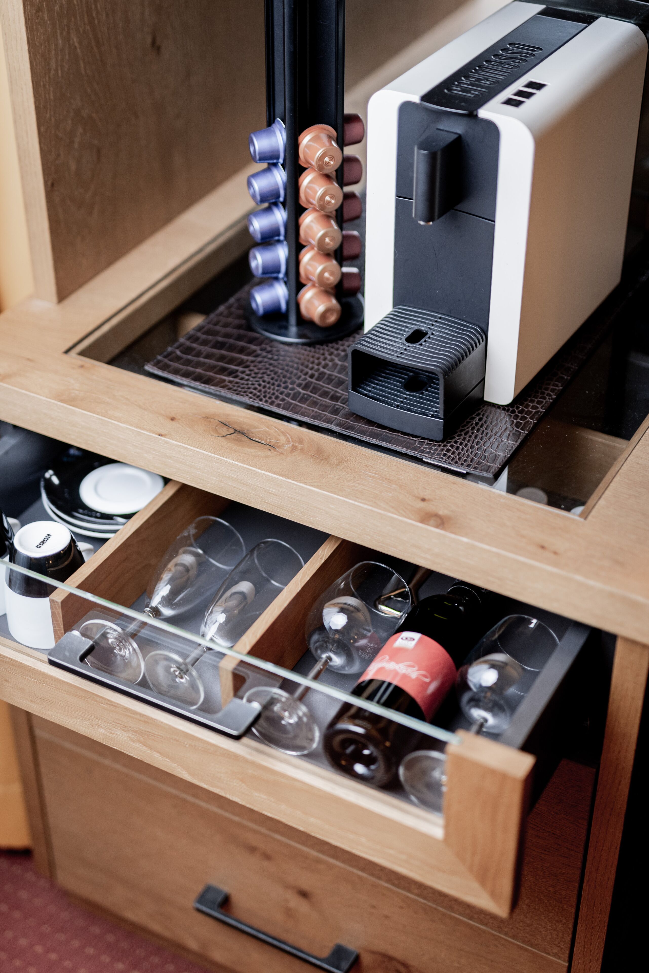 Un cassetto con bicchieri da vino e bottiglie, un mini frigo per vino e una macchina per il caffè.