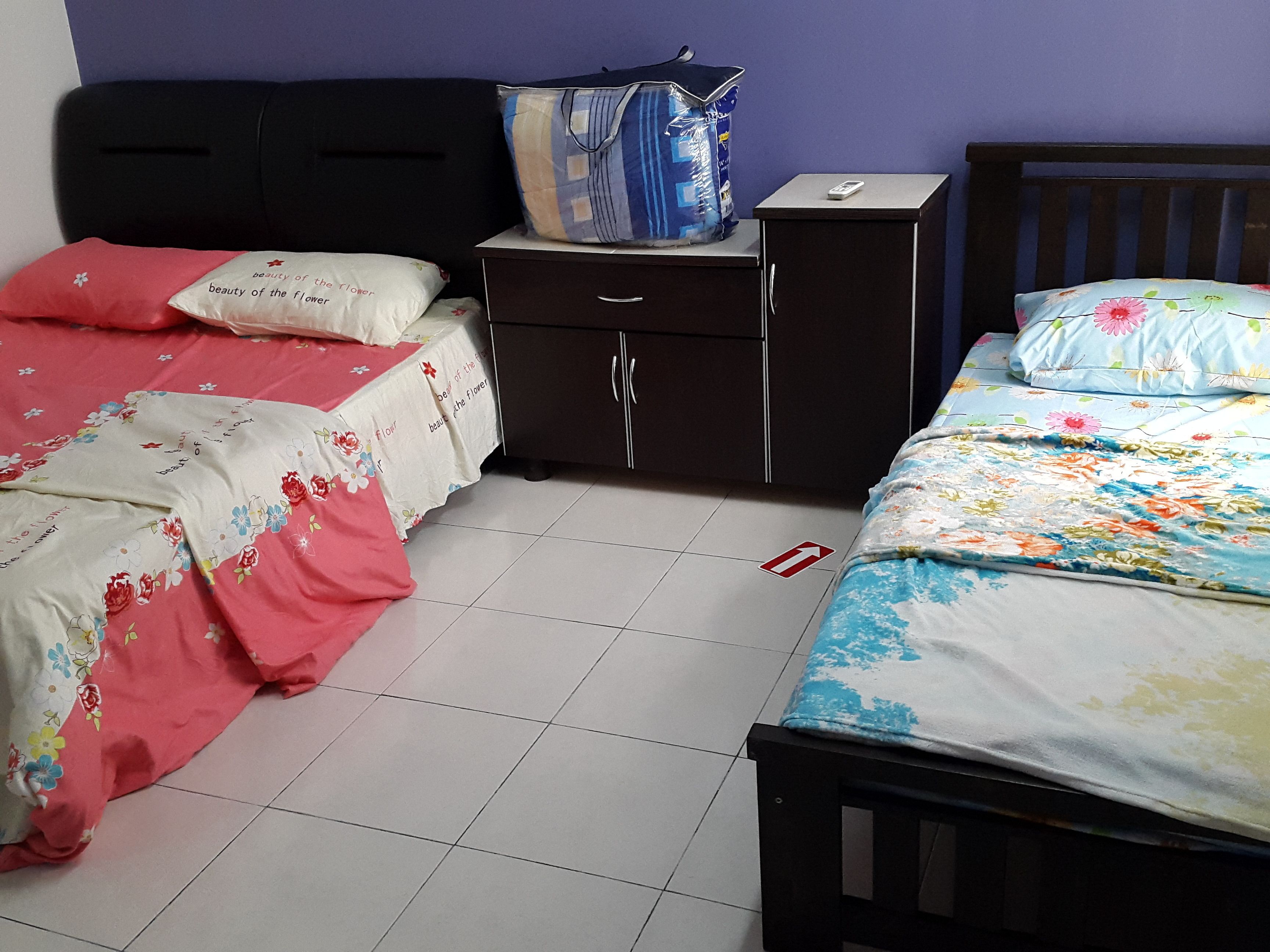 Une chambre avec deux lits simples, une table de chevet, une commode et un sac posé sur la commode.