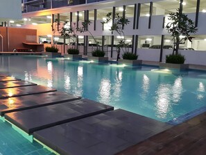 Ein Schwimmbecken mit Fliesenränder, umgeben von Kübelpflanzen und einem modernen Gebäude mit mehreren Etagen und Balkonen.
