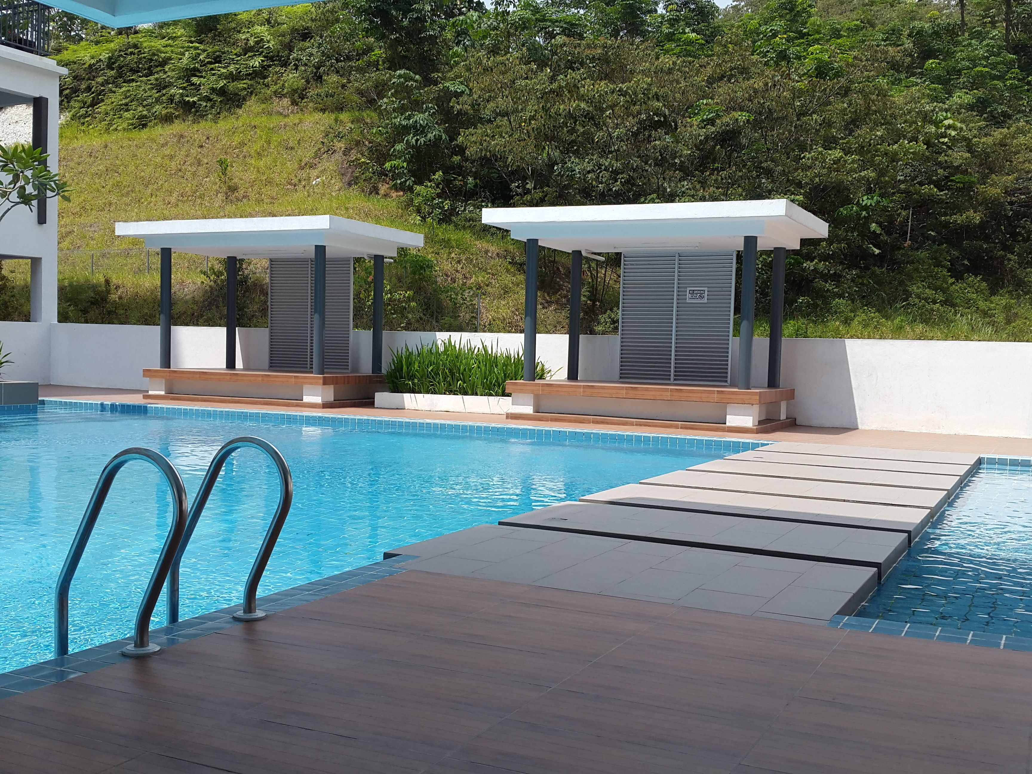 Piscina com água azul cristalina, rodeada por um deck de madeira e estruturas brancas.