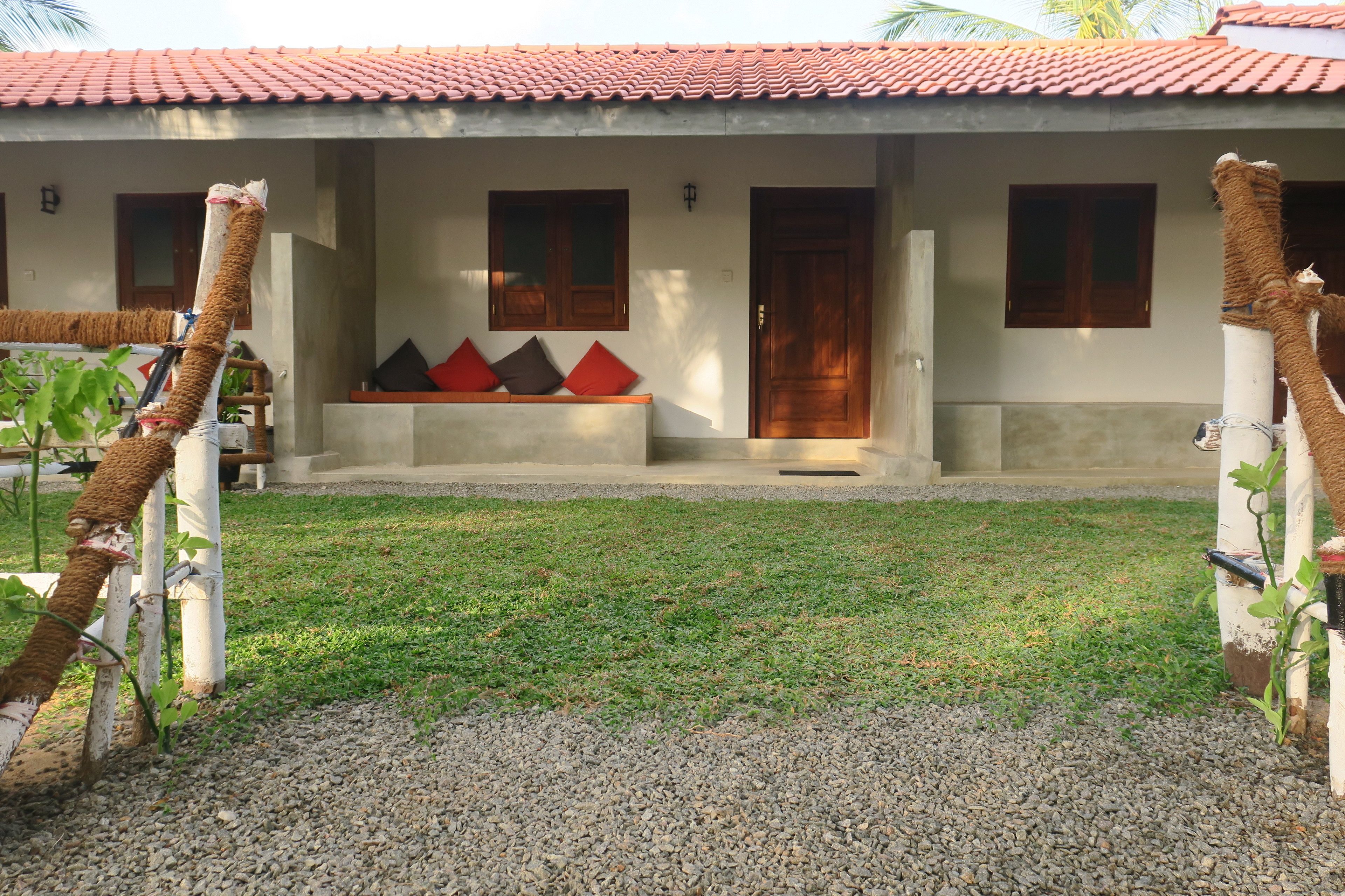 A house with a tiled roof, a porch with a bench, and a gravel driveway.