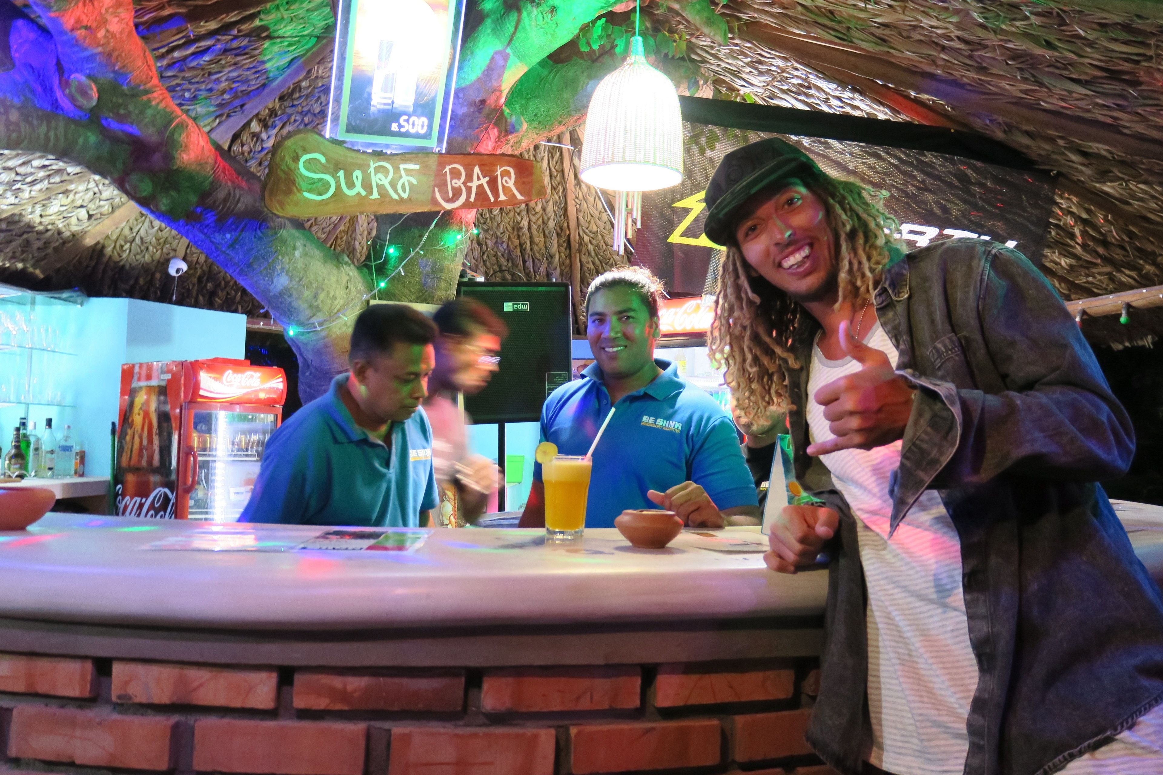 Zona de bar con un letrero que dice "Surf Bar" y un letrero de neón arriba.