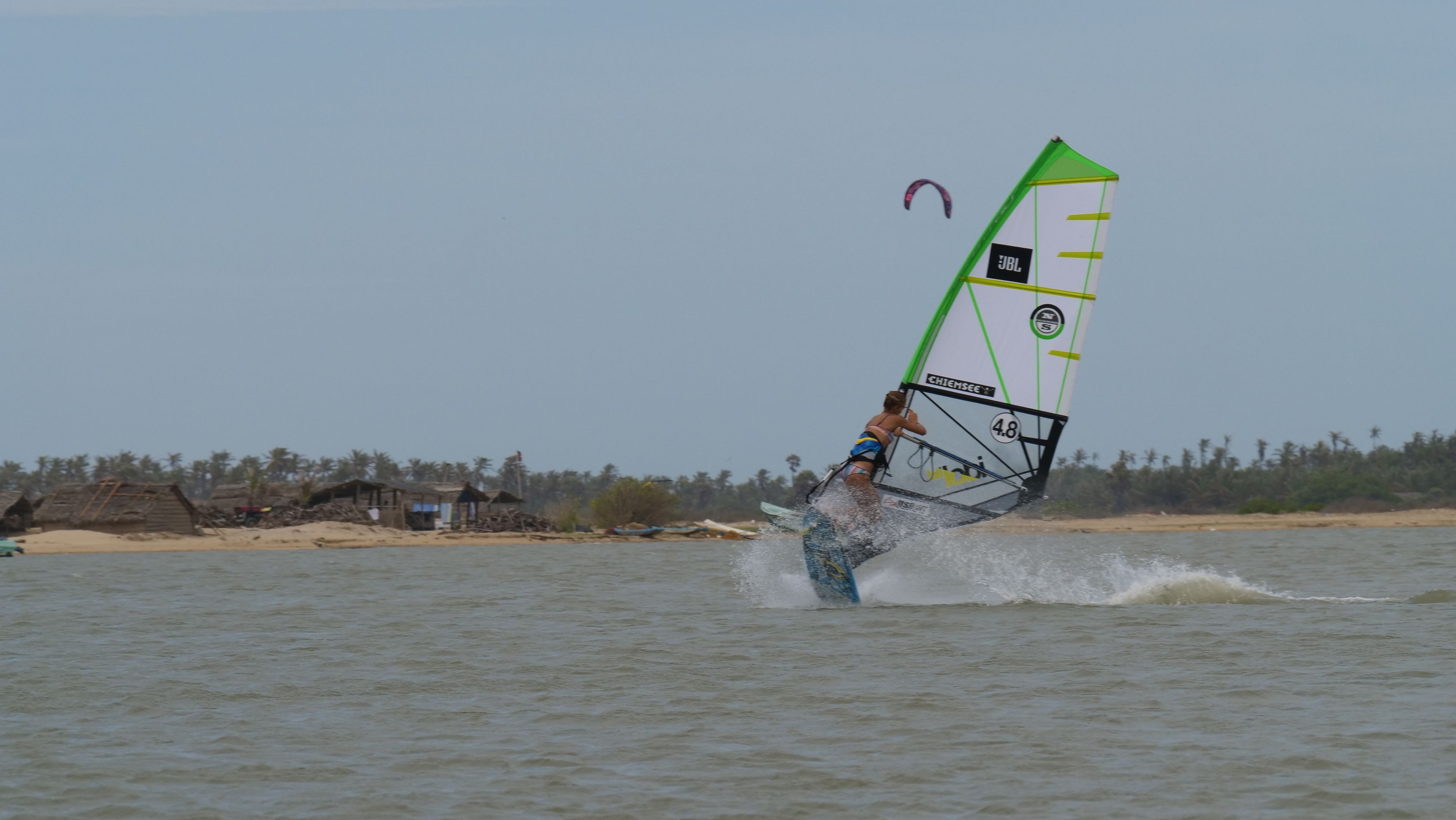 Una persona practicando windsurf en un cuerpo de agua con una vela marcada con 'JBL' y 'CHIEMSEE'.