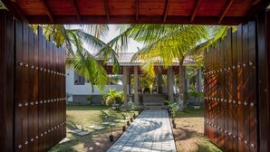 A pathway leading to a covered entrance with a wooden fence and palm trees.