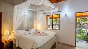 A bedroom with a canopy bed, bedside lamps, and a view of the outdoor garden.