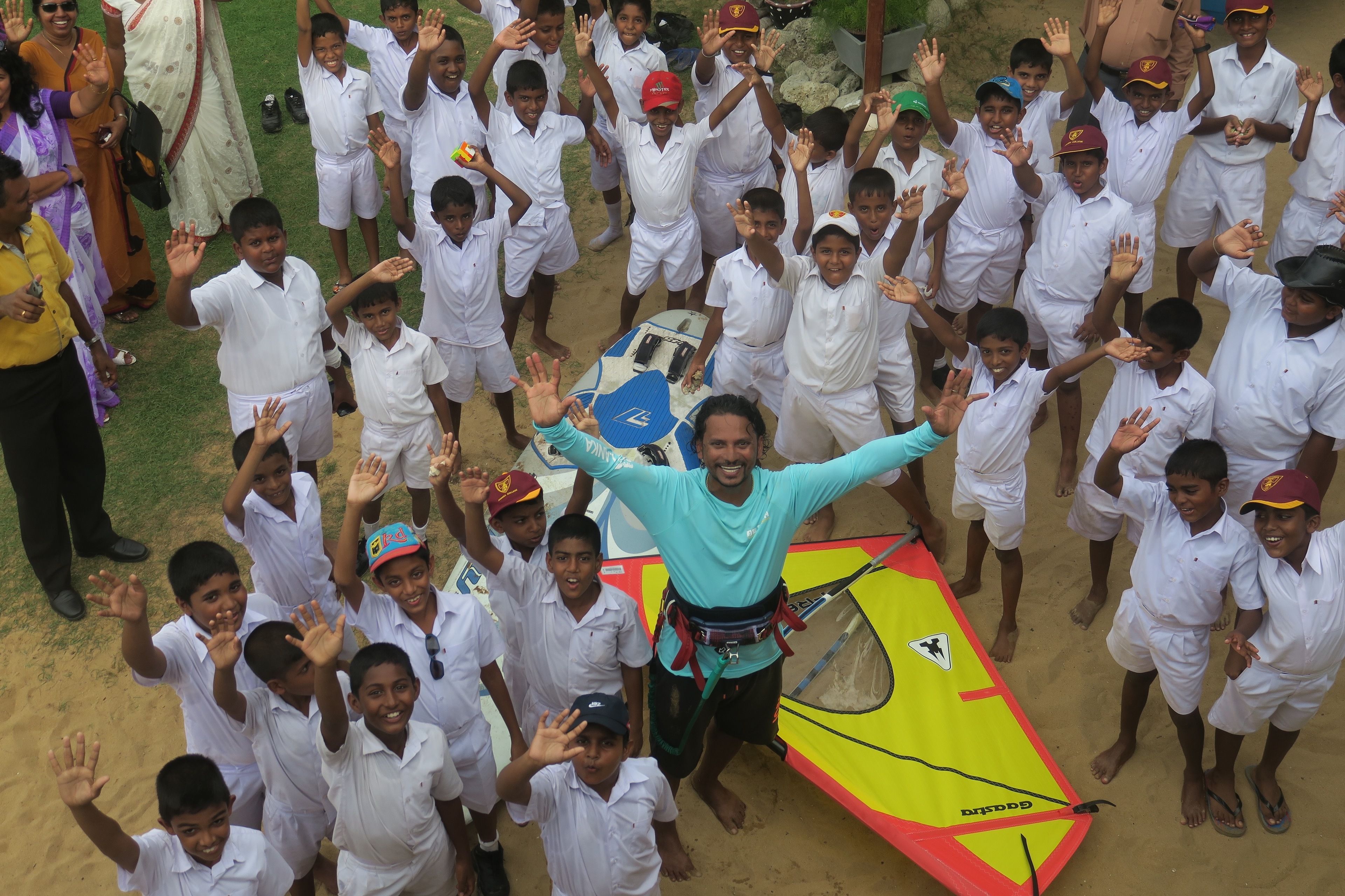 A group of children in white uniforms gathered around a man with a surfboard.