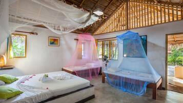 A room with two beds, each covered with a mosquito net. There are windows with wooden frames, a ceiling fan, and a painting on the wall.