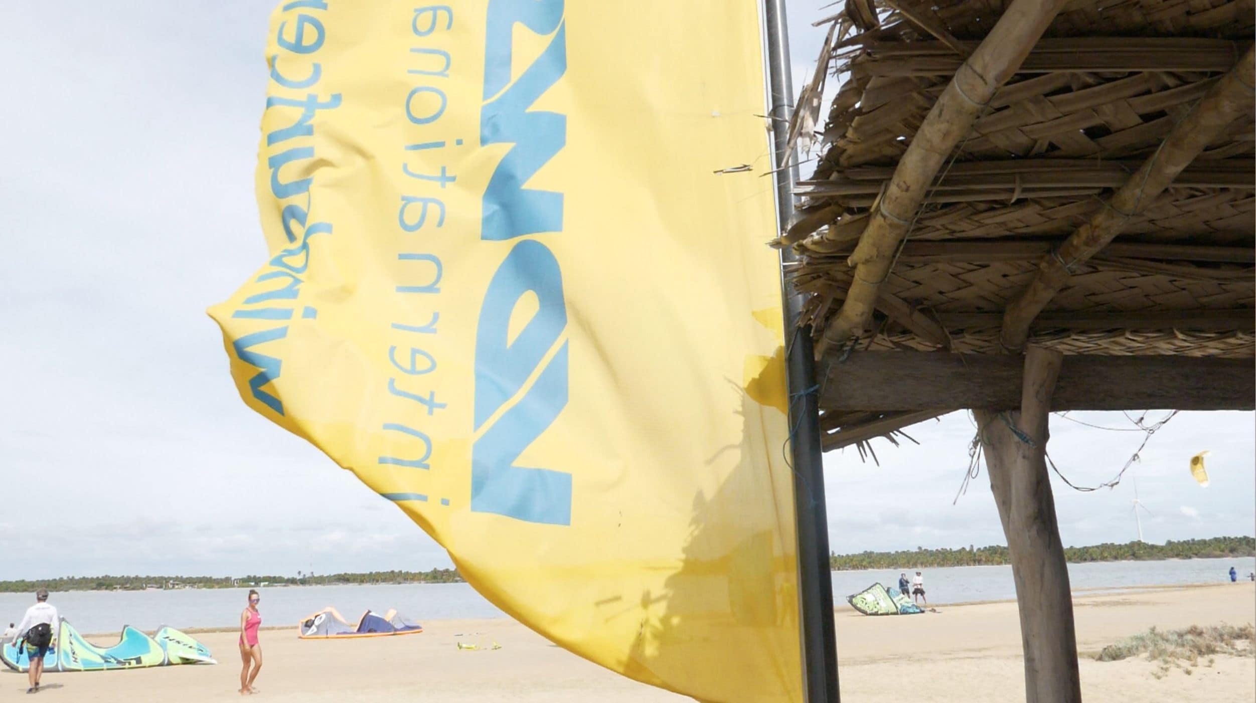Een strandzicht met een gele vlag, strandparasols en een rieten constructie.