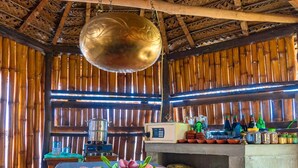 A room with a massage table, a hanging brass bowl, bamboo walls, and a counter with various bottles and jars.