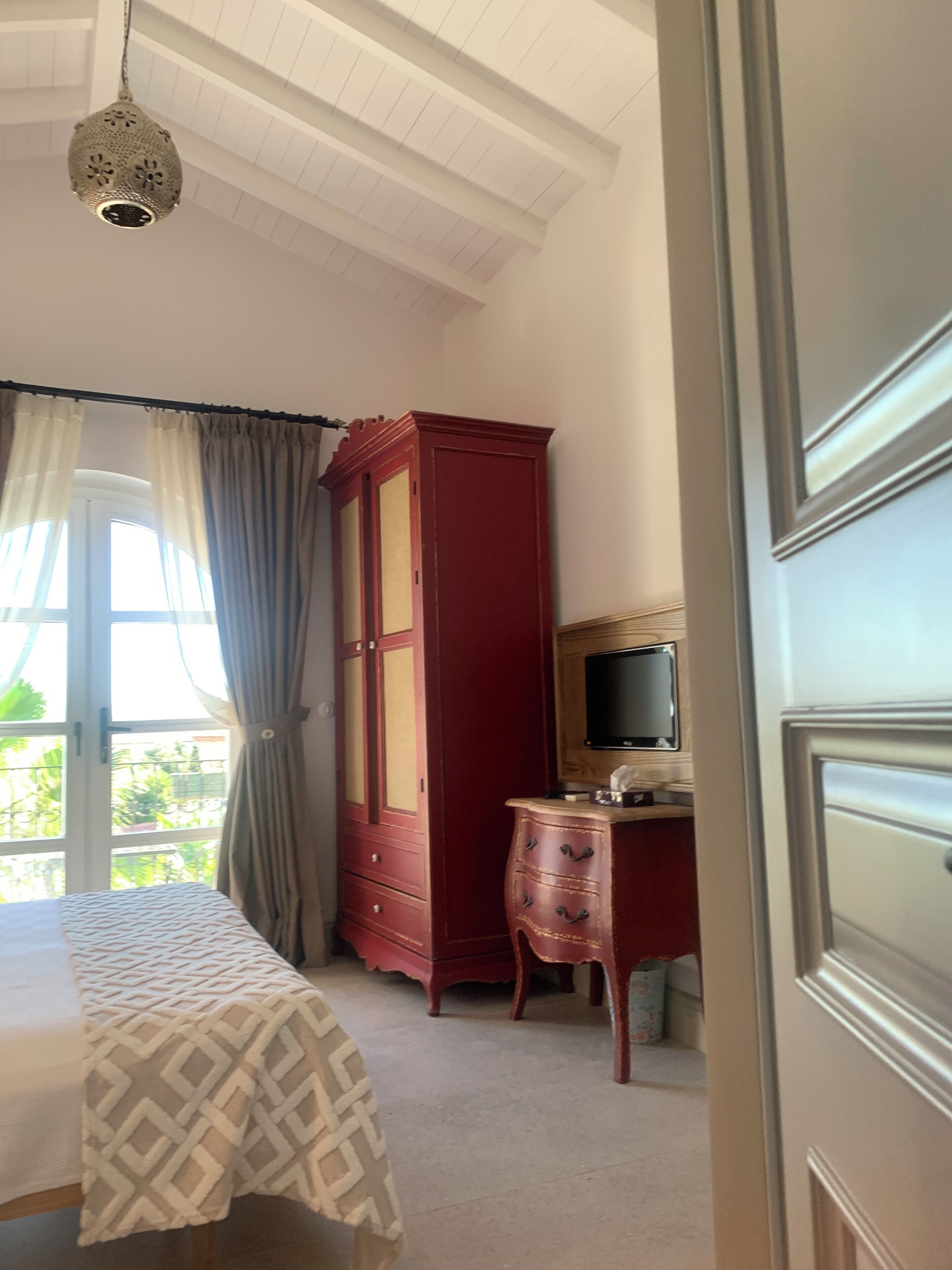 Een slaapkamer met een bed, een kledingkast, een televisie en een raam met gordijnen.