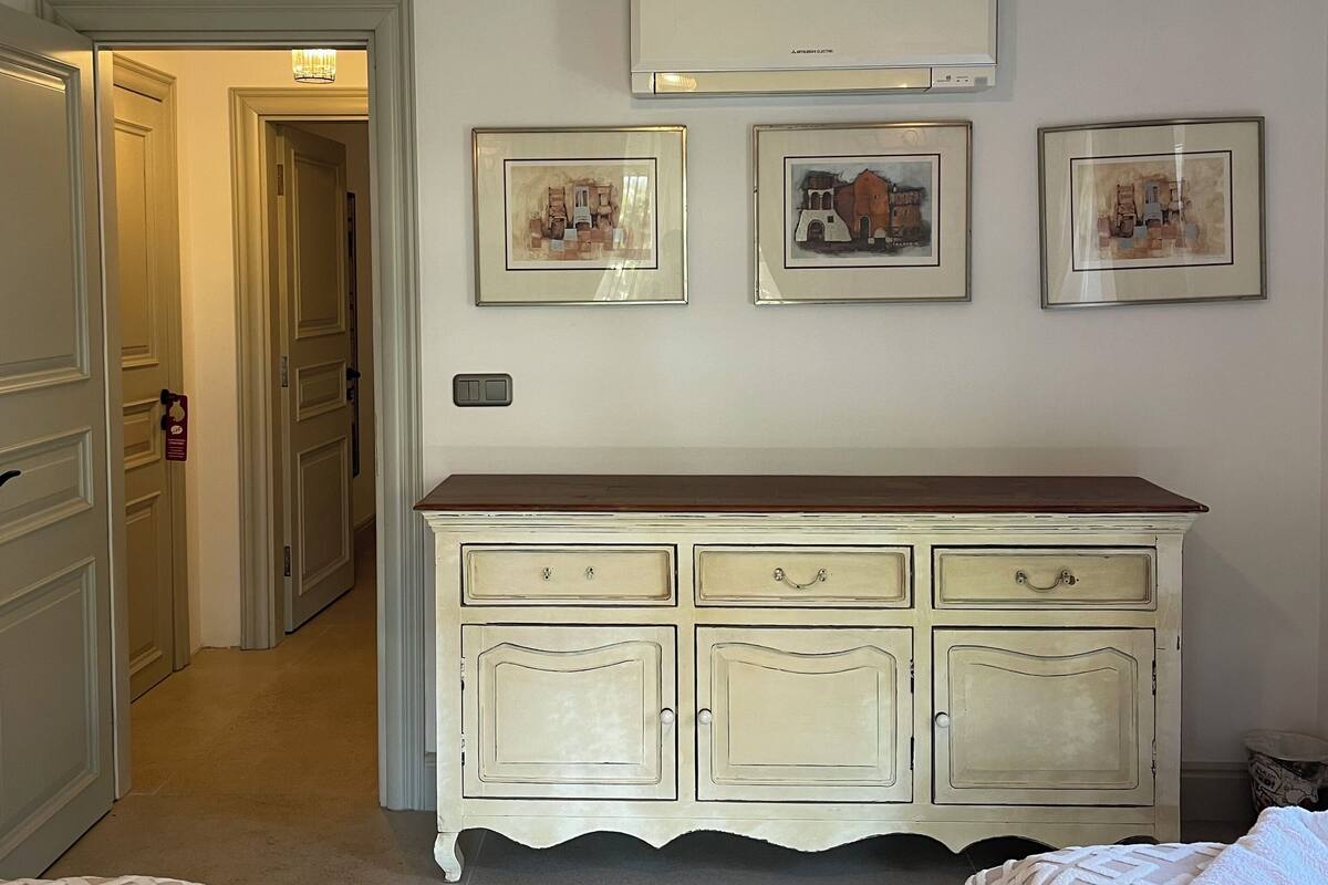 Habitación de hotel con un armario blanco, dos camas, una lámpara de techo y tres cuadros en la pared.