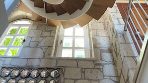 Una escalera de caracol con escalones de madera y barandillas blancas, que conduce a una habitación con paredes de piedra, una ventana y una puerta.