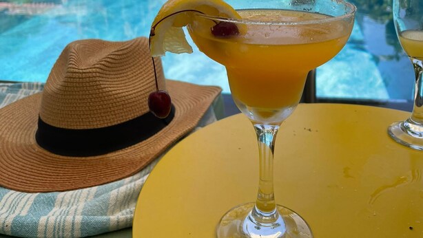 Vista de la piscina con una bebida en un vaso, un sombrero y sillas de descanso.