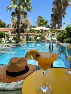 Une vue sur la piscine, avec un verre à la main, un chapeau et des chaises longues.