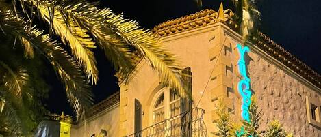 A stone building with a balcony and a neon sign.