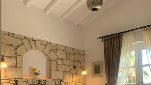Un dormitorio con pared de piedra, cama con ropa de cama estampada, lámpara colgante y vistas al exterior a través de una ventana.