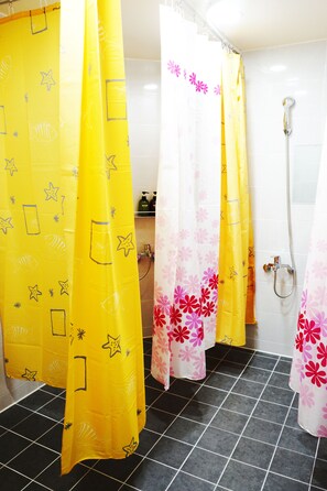 A bathroom with black tiled floors, yellow and pink shower curtains with star patterns, and a white tiled wall. - Onna Guesthouse - Hostel (Daegu)