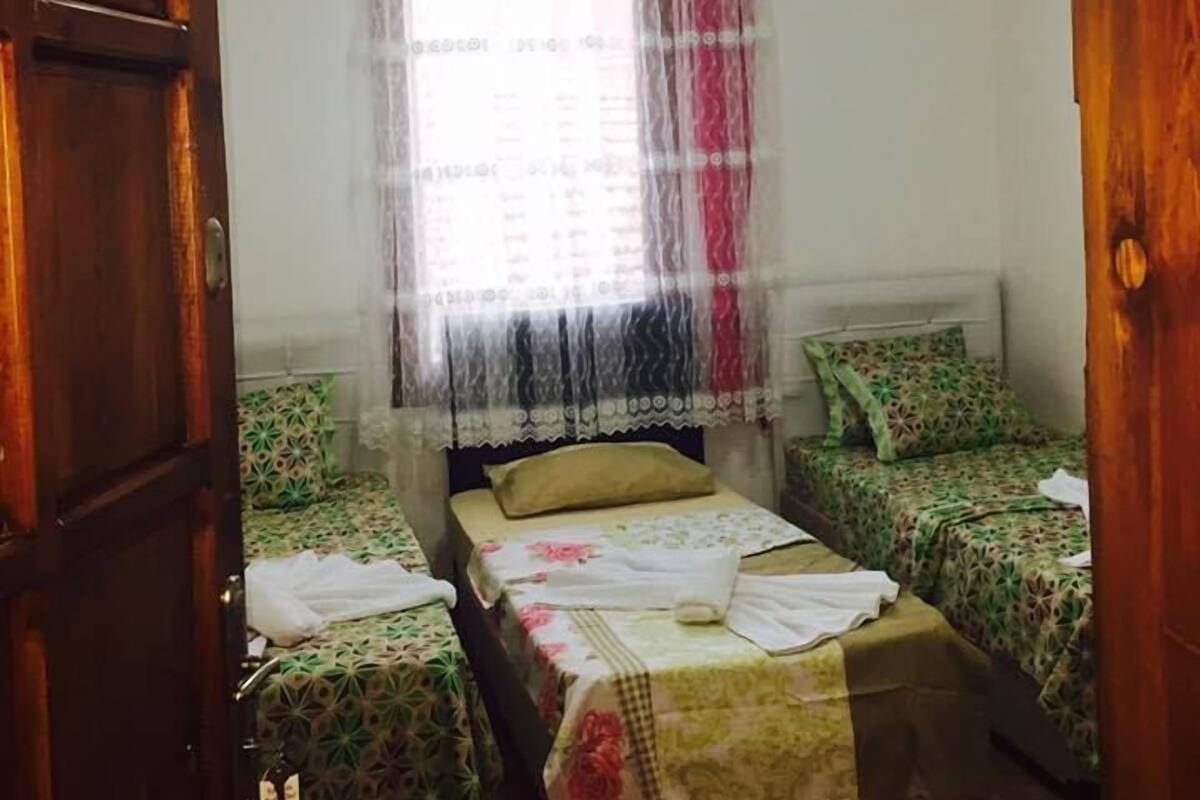 Una habitación con dos camas individuales, una puerta de madera, una ventana con cortina translúcida y un candelabro.
