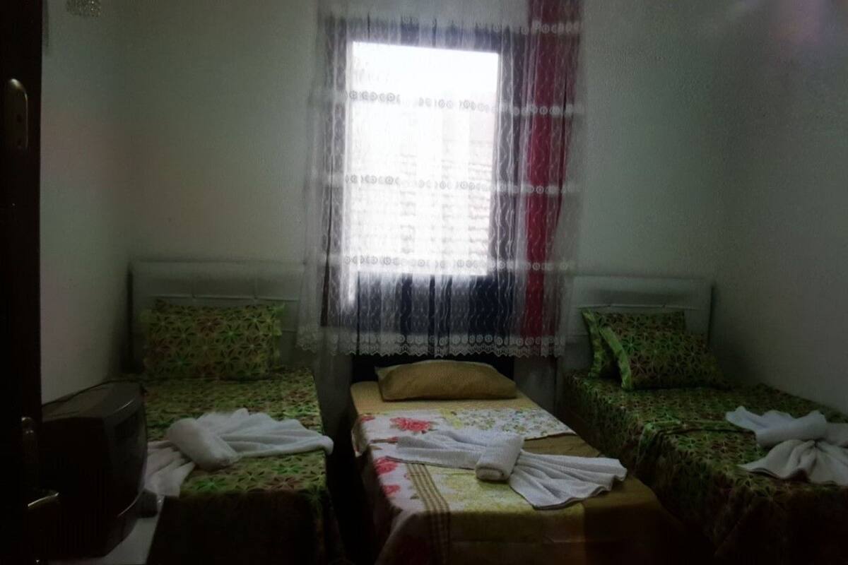 Una habitación con dos camas individuales, una mesita y una ventana con cortina translúcida.