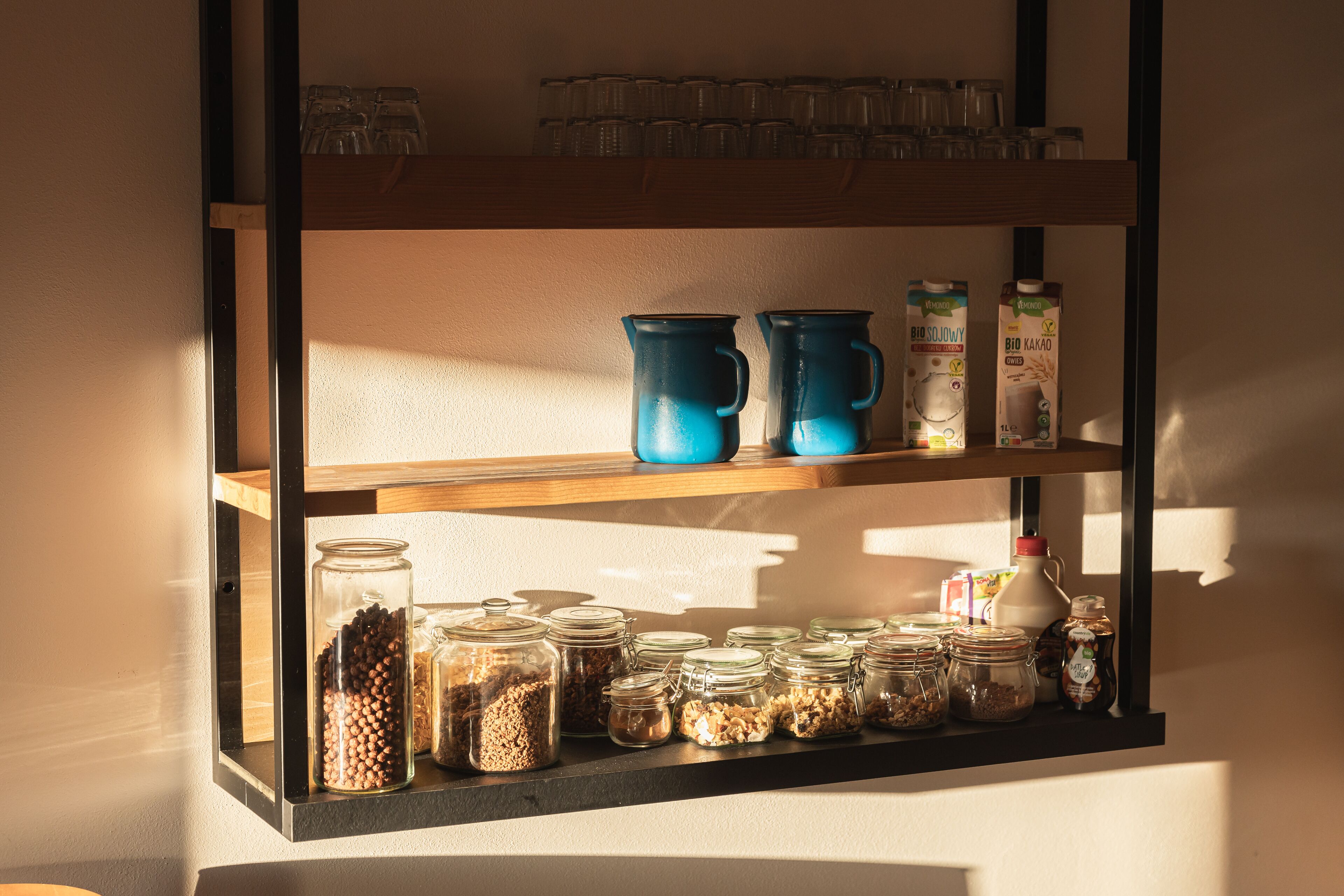 A shelf with various containers and kitchenware, including jars and mugs.