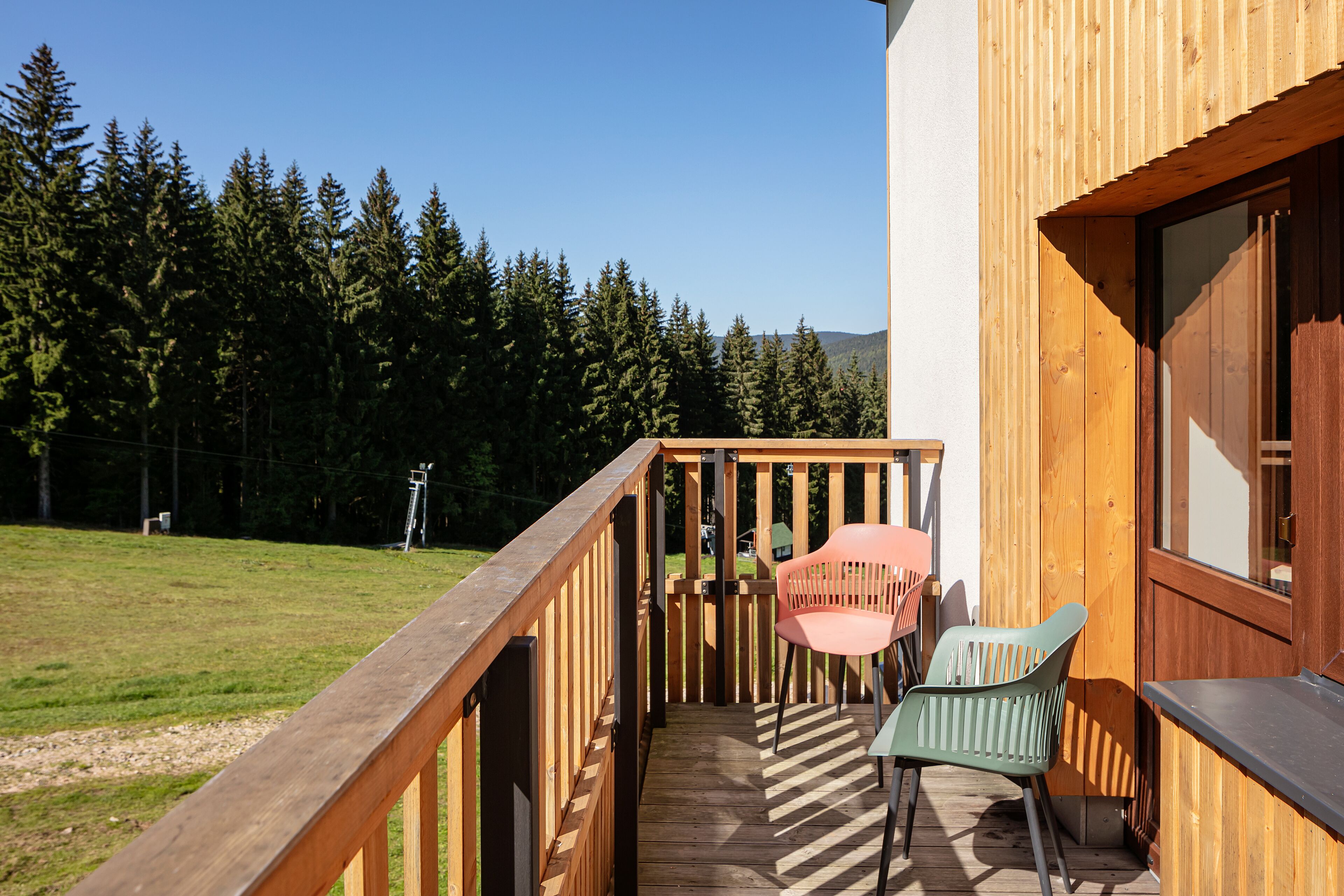 A wooden deck with a railing, two chairs, and a table.