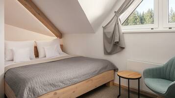 Une chambre à coucher avec un lit en bois, une couvre-lit matelassée grise, une petite table ronde et un fauteuil turquoise.
