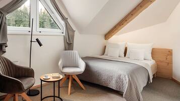 Een slaapkamer met een bed, twee stoelen, een klein tafeltje, een vloerlamp en een raam met gordijnen.