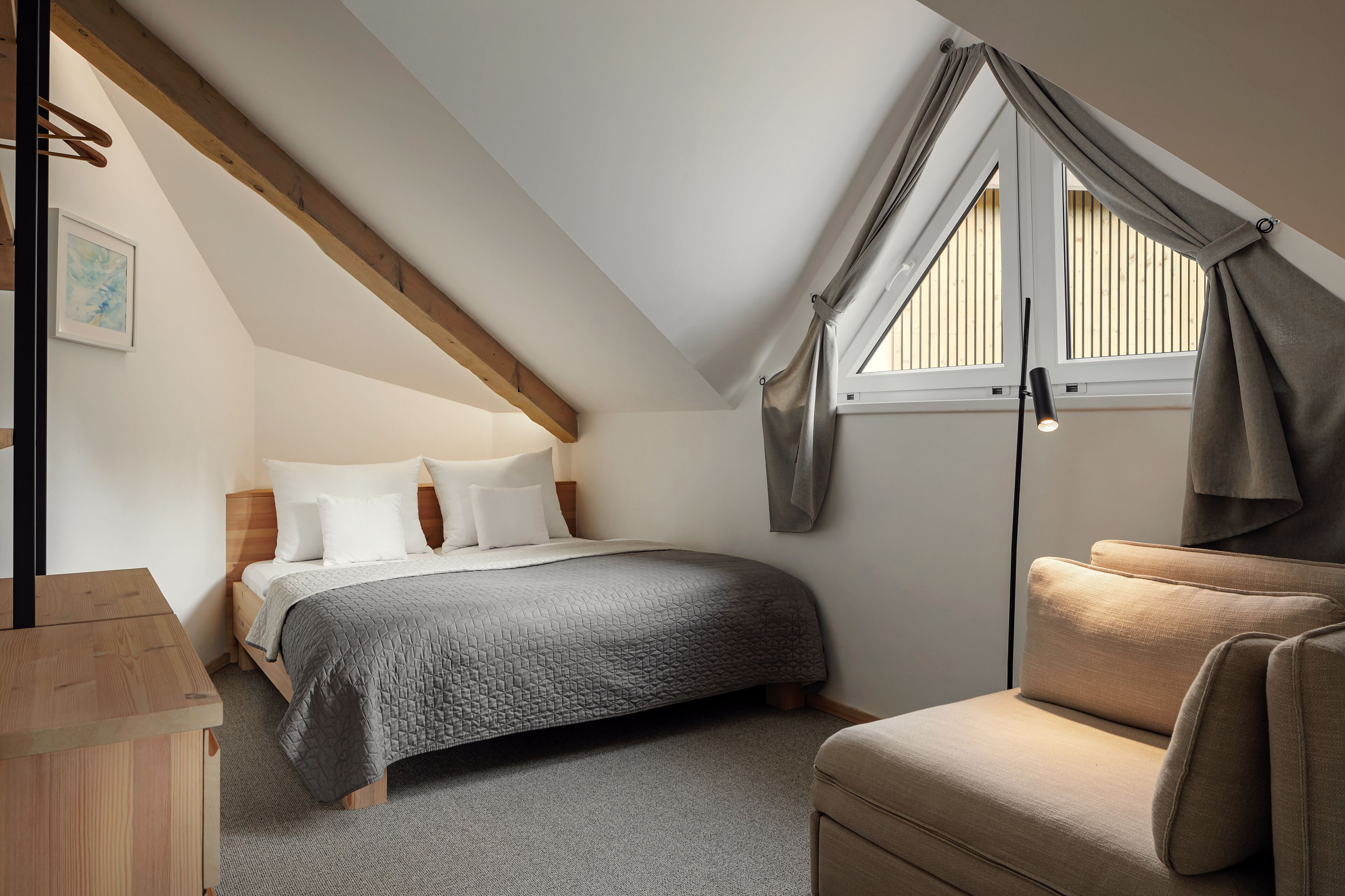 A bedroom with a bed, a chair, a desk, and a window with curtains.