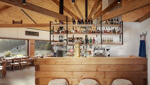 A bar area with wooden shelves stocked with various bottles and glasses, wooden benches with sheepskin covers, and a large window offering a view of the outdoors. - Ski & Spa Bellevue Harrachov (Harrachov)