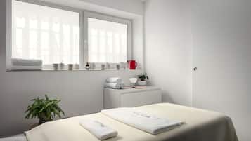 Habitación de hotel minimalista con un ventanal grande, una mesita de noche con artículos de aseo, una cama con una toalla doblada con cuidado y una planta en maceta.